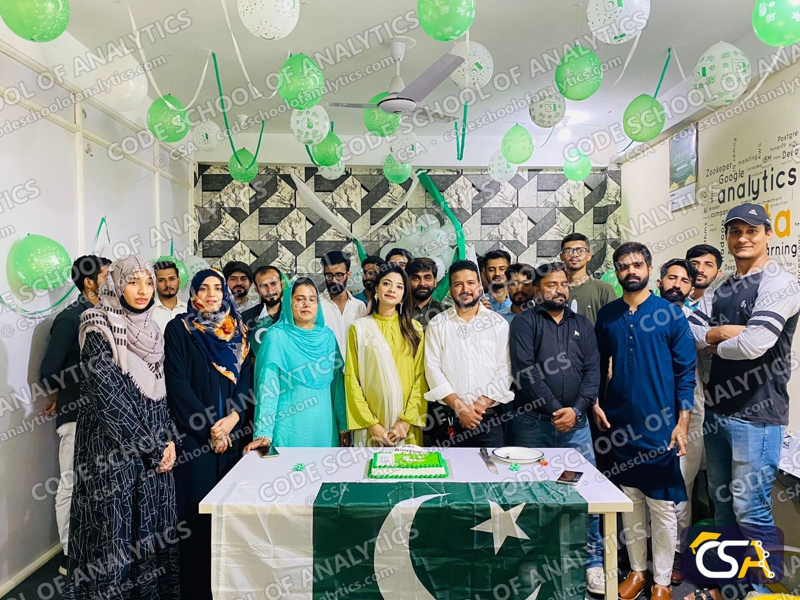 Group photo behind the Pakistan flag and celebration cake at CSA